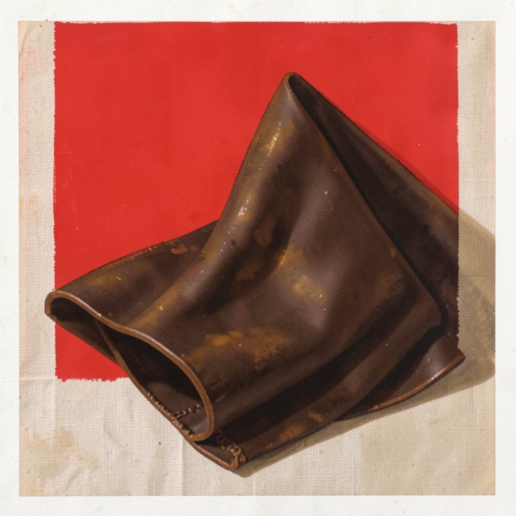 Folded dark chocolate-brown leather material on a pale linen surface with soft amber highlights